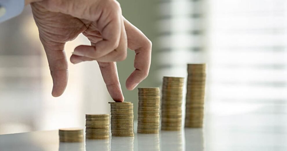 Hand placing a coin on a rising stack of coins, illustrating financial growth and saving.