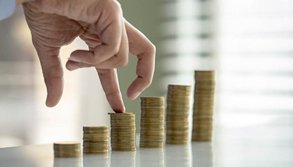 Hand placing a coin on a rising stack of coins, illustrating financial growth and saving.