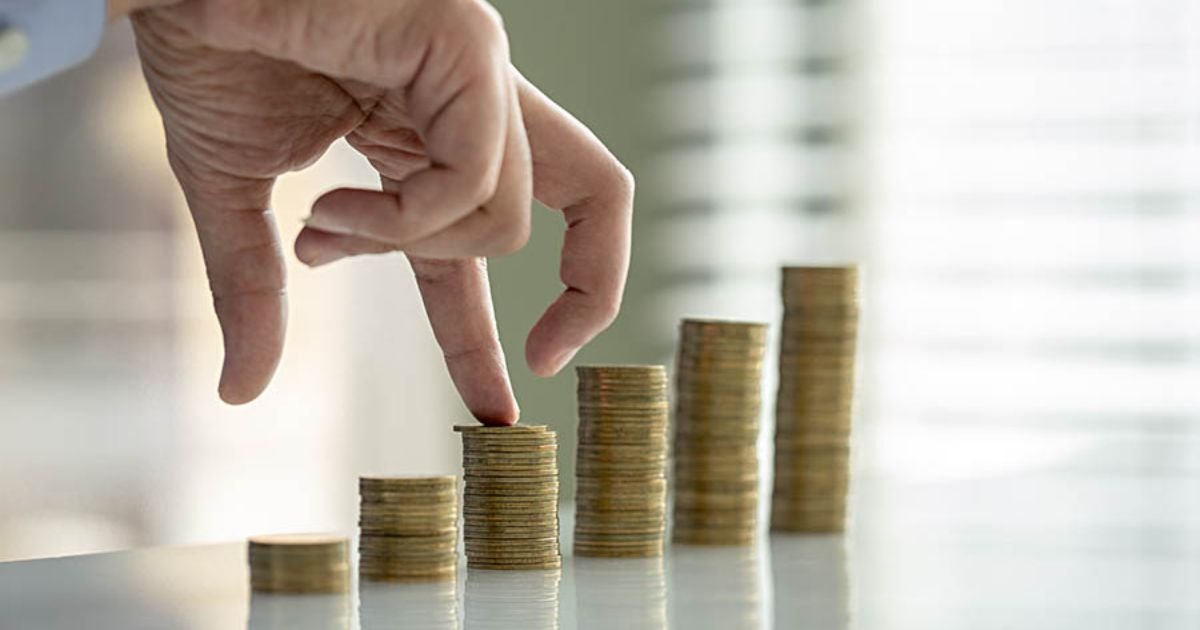 Hand placing a coin on a rising stack of coins, illustrating financial growth and saving.